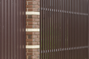 Brick column with a fence made of brown metal profiles