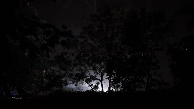 Lightening flashes during rainstorm while exploded transformer burns and emits bright orange red blue white lights on cold wet rainy New Jersey night