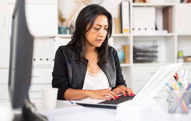 Portrait of confident latin american female office employee during daily work with laptop and...
