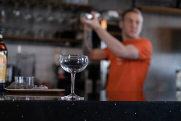 stylish young man hipster in orange t-shirt making mixing a cocktail in a dark loft cafe. alcohol drink in modern bar