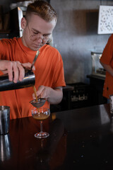 Barman is making cocktail at night club. stylish young man mixing a cocktail in a dark loft cafe. alcohol drink in modern bar. male bartender