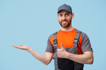 Positive worker man stands on blue background points his finger up and to side in empty place