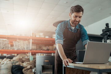 Business owner of small coffee factory working laptop on background of coffee roasting machine