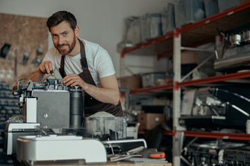 Man worker repair a coffee machine in own workshop and looking camera