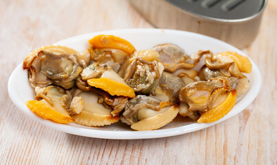 Seafood appetizer. Canned natural shellfish served on white plate on wooden surface..