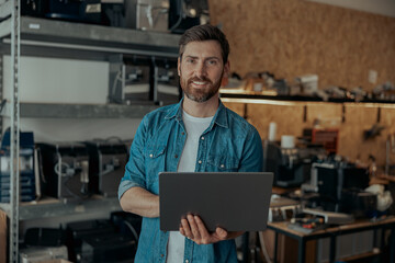 Business owner standing with laptop on warehouse with coffee machines