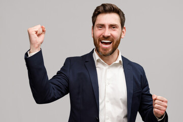 Happy businessman in suit rejoices in achieving goal doing winner gesture clenching fists 