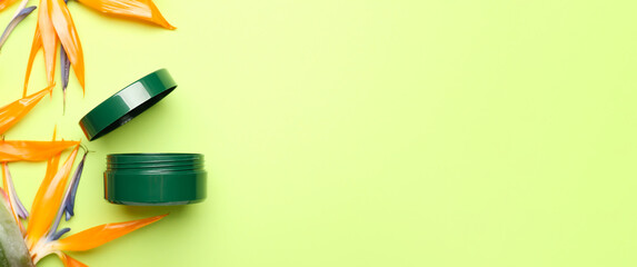 Jar of cosmetic cream and strelitzia flowers on green background with space for text