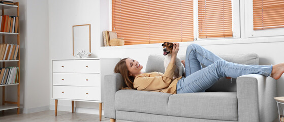 Pretty young woman with Jack Russel terrier lying on grey sofa at home