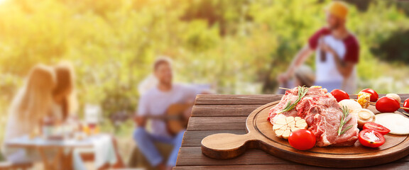 Board with raw meat and vegetables for barbecue party on wooden table outdoors