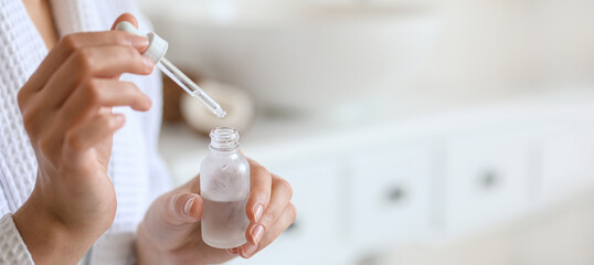 Young woman with bottle of essential oil in bathroom, closeup