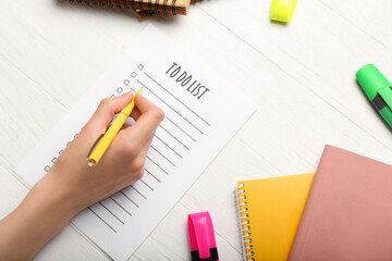 Female hand, to-do list and colorful stationery on light wooden background, closeup