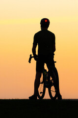 Obraz na płótnie Canvas Silhouette of helmeted bicycle rider against a sunset orange sky.