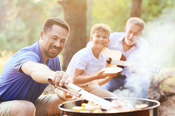 Handsome man cooking food on grill with his family at barbecue party