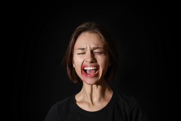 Bruised young woman screaming on black background. Violence concept