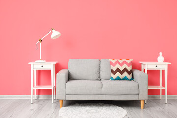 Comfortable sofa and modern lamp on table near pink wall