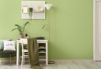 Interior of room with comfortable workplace and pegboard near green wall