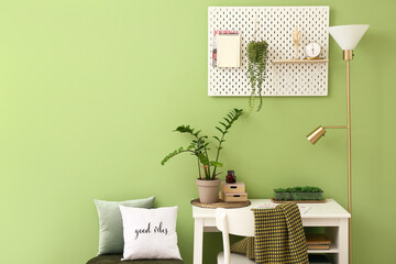 Comfortable workplace and pegboard near green wall in room