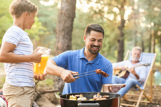 Handsome Man Putting Grilled Meat On Plate At Barbecue Party