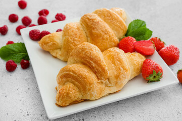 Plate of delicious croissants with berries on light background