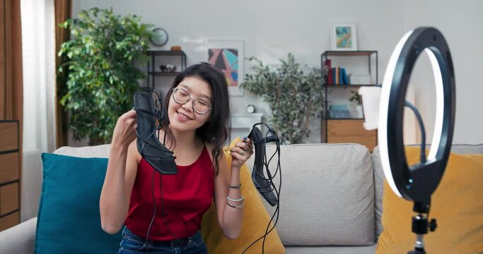 Fashion blogger woman sitting on couch showing high heel shoes in front of camera. Influencer stylist showing off fashionable footwear while filming vlog episode for channel.