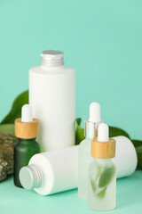 Bottles of natural serum, cosmetics and plant leaves on turquoise background