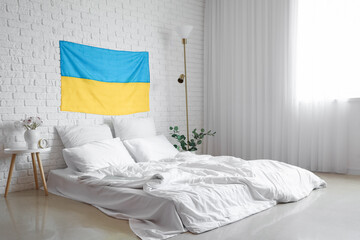 Interior of light bedroom with flag of Ukraine and comfortable bed