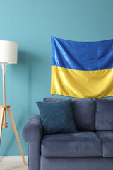 Comfortable sofa, floor lamp and flag of Ukraine hanging on color wall
