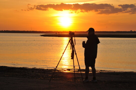 Horizontal format of a photographer taking pictures from a tripod at sunset on the beach