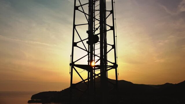 Amazing closeup sunset drone view of silhouette of cell tower. Wireless connection. Spectacular view of cellular tower with mountains and sea in the background. 5G network. Сell site