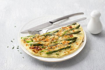 Delicious omelette with asparagus and cheese on a white plate on a light gray background, top view. Homemade vegetarian food