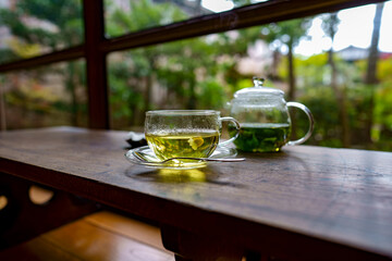 古民家カフェにある歴史を感じる寺子屋机と硝子ポットの中に入ったフレッシュハーブティとカモミールの花が泳ぐガラス製のティーカップ