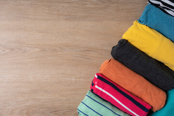 close up of rolled colorful t shirt clothes on wooden table background, travel concept