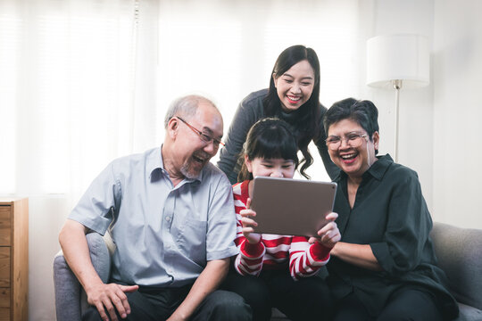 Big Asian family looking at tablet, Happy and fun grandparents with technology, grandfather, grandmother and young girls at home
