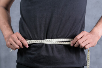 Close-up of a man measuring belly with measuring tape. Diet and weight problems.