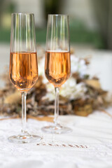 two tall and narrow glass goblets with sparkling wine on a white vintage tablecloth