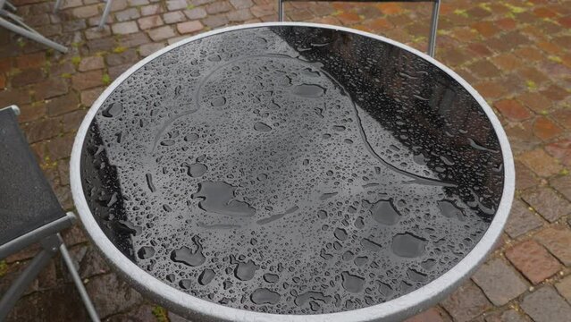 Heart shape drawn on wet glass surface of small table, large and small water drops around. Table stand at the street, typical outdoor terrace of cafe. Romantic mood at rainy weather