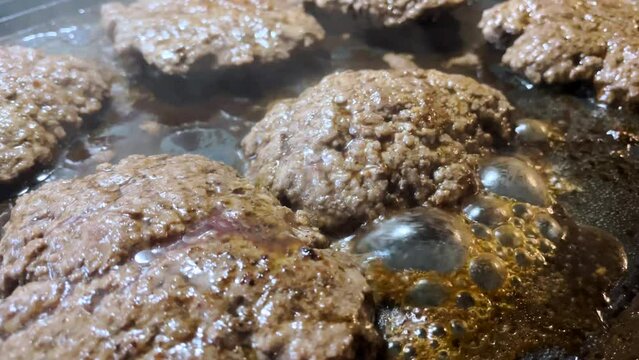 Hamburger patties frying on a griddle grease bubbles