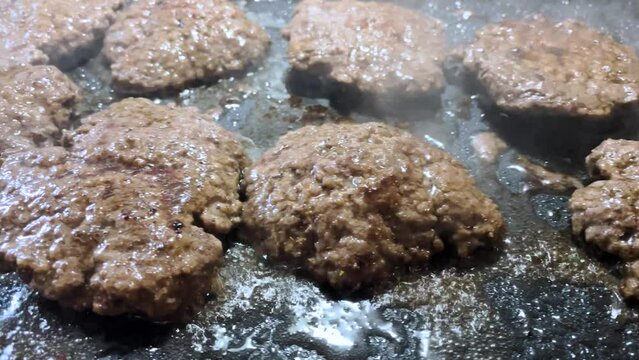 Hamburger patties frying on a griddle left pan hand held