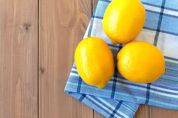 three fresh lemons on a wooden table. there is a cotton kitchen towel next to it
