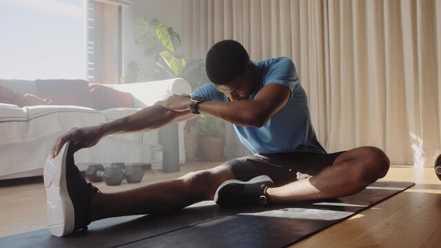 Young African American black male stretching his legs and hamstrings on a gym mat in living room, after exercising in living room working out at home
