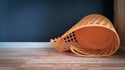 Empty and broken plastic laundry basket orange colored indoors. It's not useless. It can fix and...