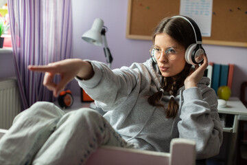 A teenage girl listens to music and gestures with her hands. Wireless headphones.