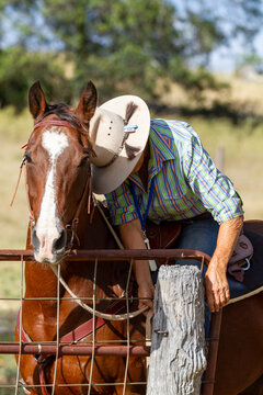 A country lady in her sixties opening a gate whilst riding a horse.