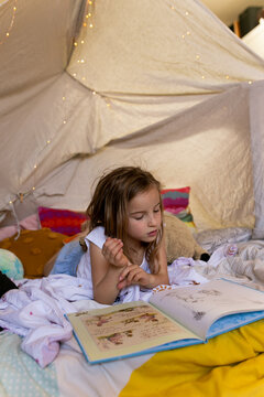Girl reading a story book in a tent cubby house