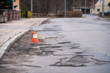 Damaged asphalt pavement road with potholes and traffic cone