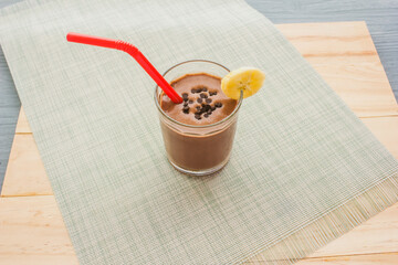 Chocolate banana smoothie topping sprinkled with chocolate chips banana slices on a wooden floor.