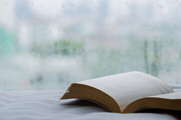 Book put on bed in morning with rain drop on window. Stay home and relaxing concept.