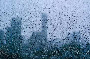 Rain drop on glass window at day time in monsoon season with blurred city buildings background.