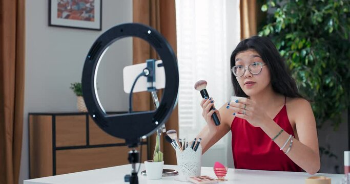 A popular makeup blogger records vlog, video for social media, influencer collaborates with cosmetics brand, girl reviews a rice powder she applies to face, she likes the smell of the product